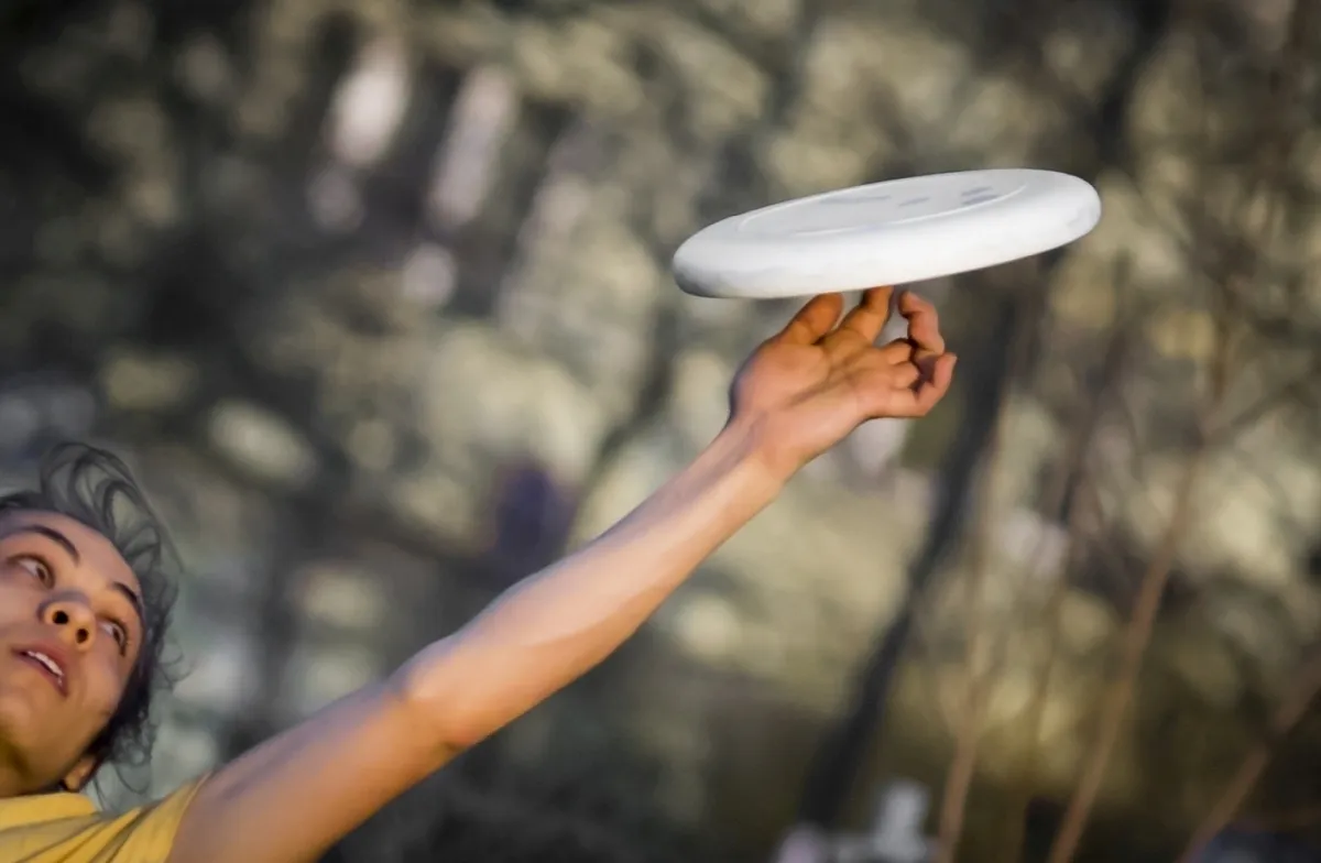 Hand spinning a white frisbee above a blurred face